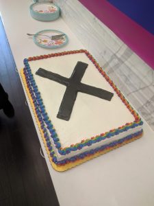 A large rectangular cake, with gorgeous rainbow icing around the edges, and a large X in black right in the middle.